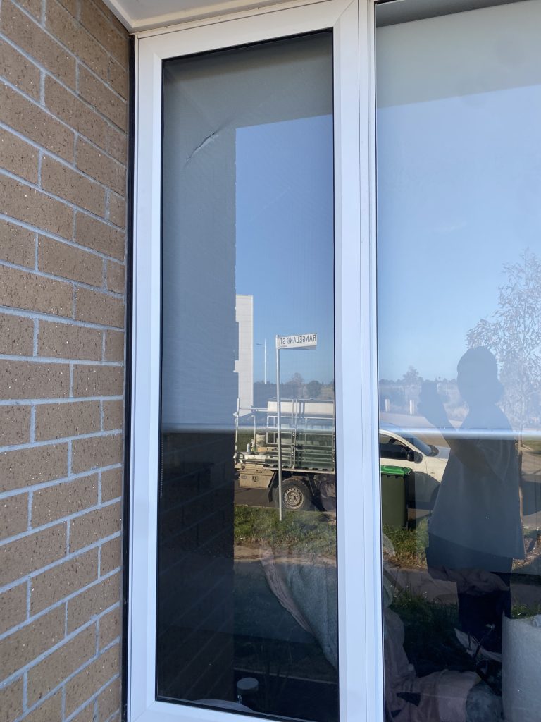 A person stands in front of a white window, gazing outside with a thoughtful expression.