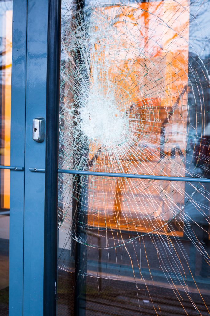 A broken glass door featuring a shattered window, with jagged edges and fragments scattered on the ground.